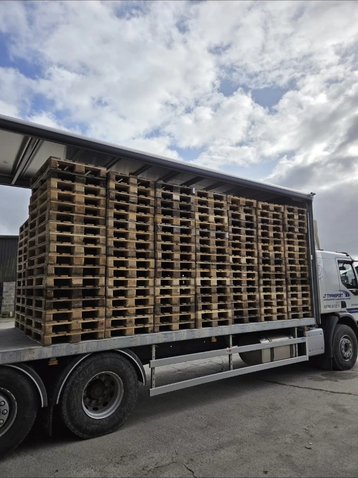 Stacks of wooden pallets on a JT curtainsider truck.