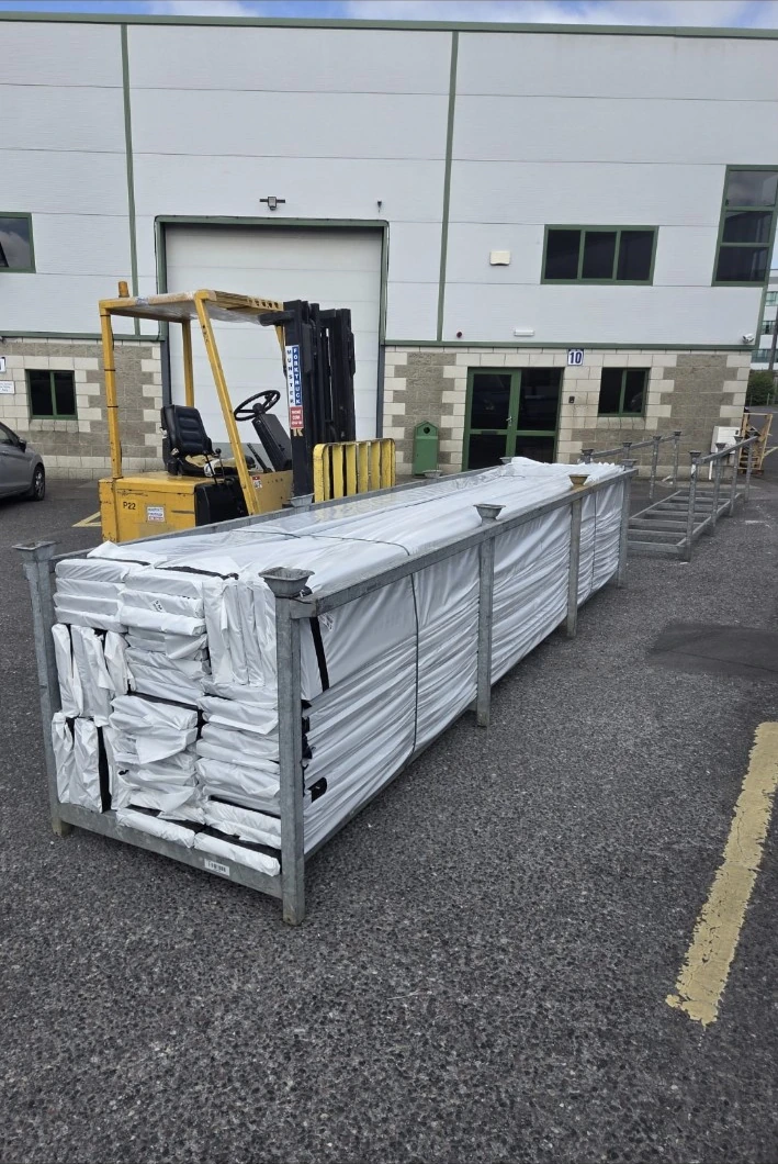 Wrapped long materials in a metal stillage outside an industrial building, with a forklift nearby.
